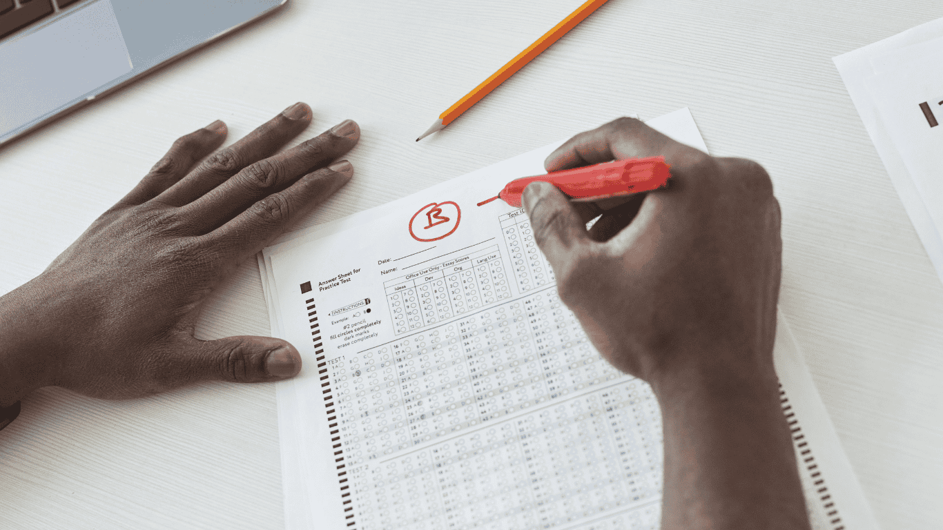 A person grading a multiple-choice answer sheet with a red marker, circling a letter 'B' at the top.