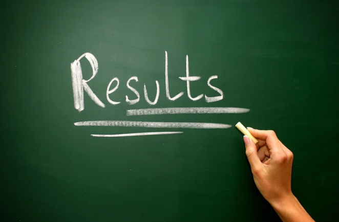 Hand writing the word 'Results' on a green chalkboard with white chalk, with the text underlined. Symbolizing exam results