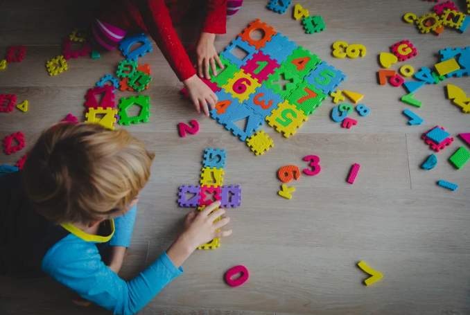 Children playing with colorful foam puzzle pieces shaped like numbers and letters on a wooden floor, engaging in a fun and educational activity.